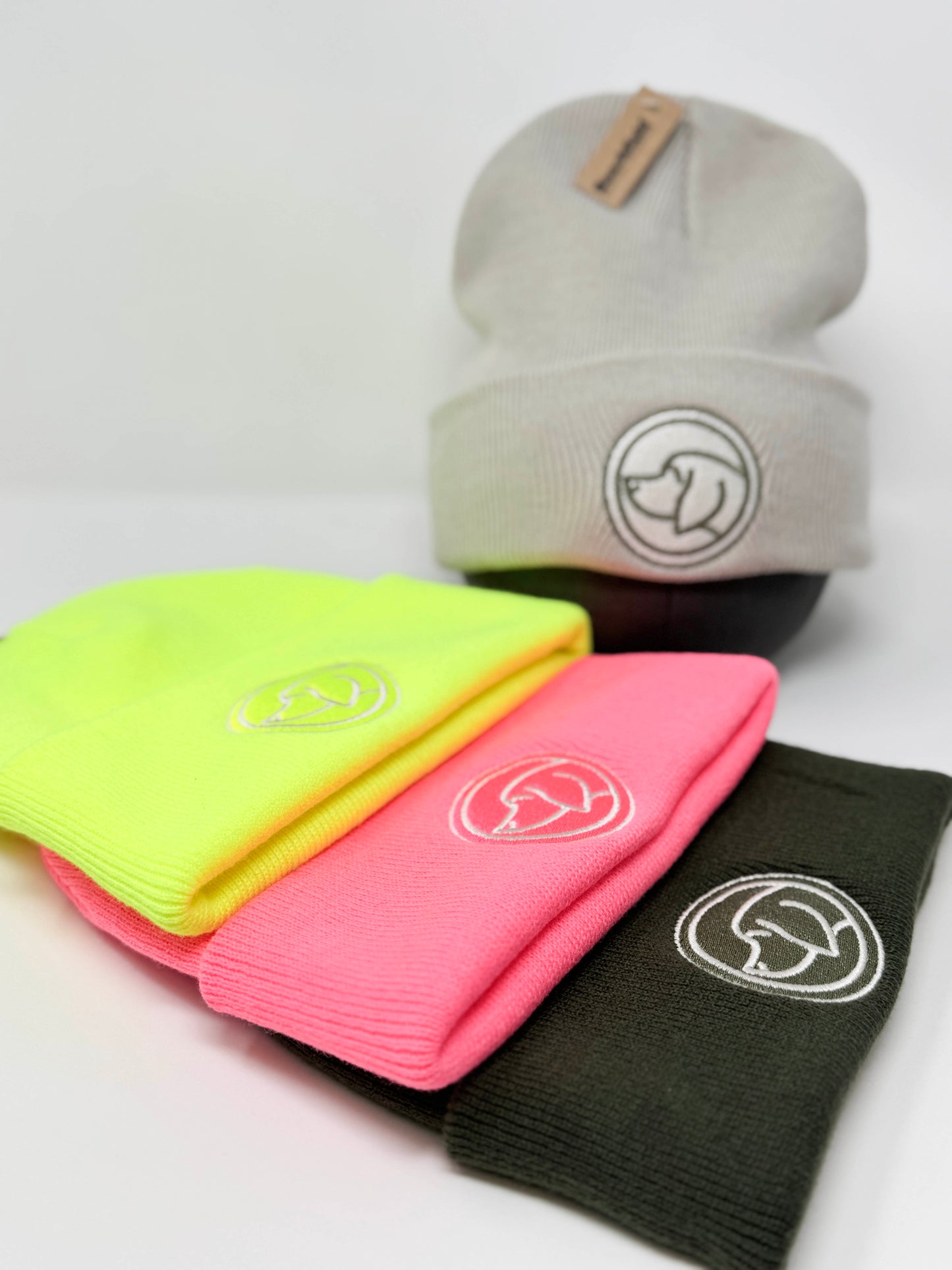 Branded beanie hats in Army Green, Neon Pink, Neon Yellow laid flat, with Stone beanie on mannequin head, branded with dog logo, unisex winter hats.