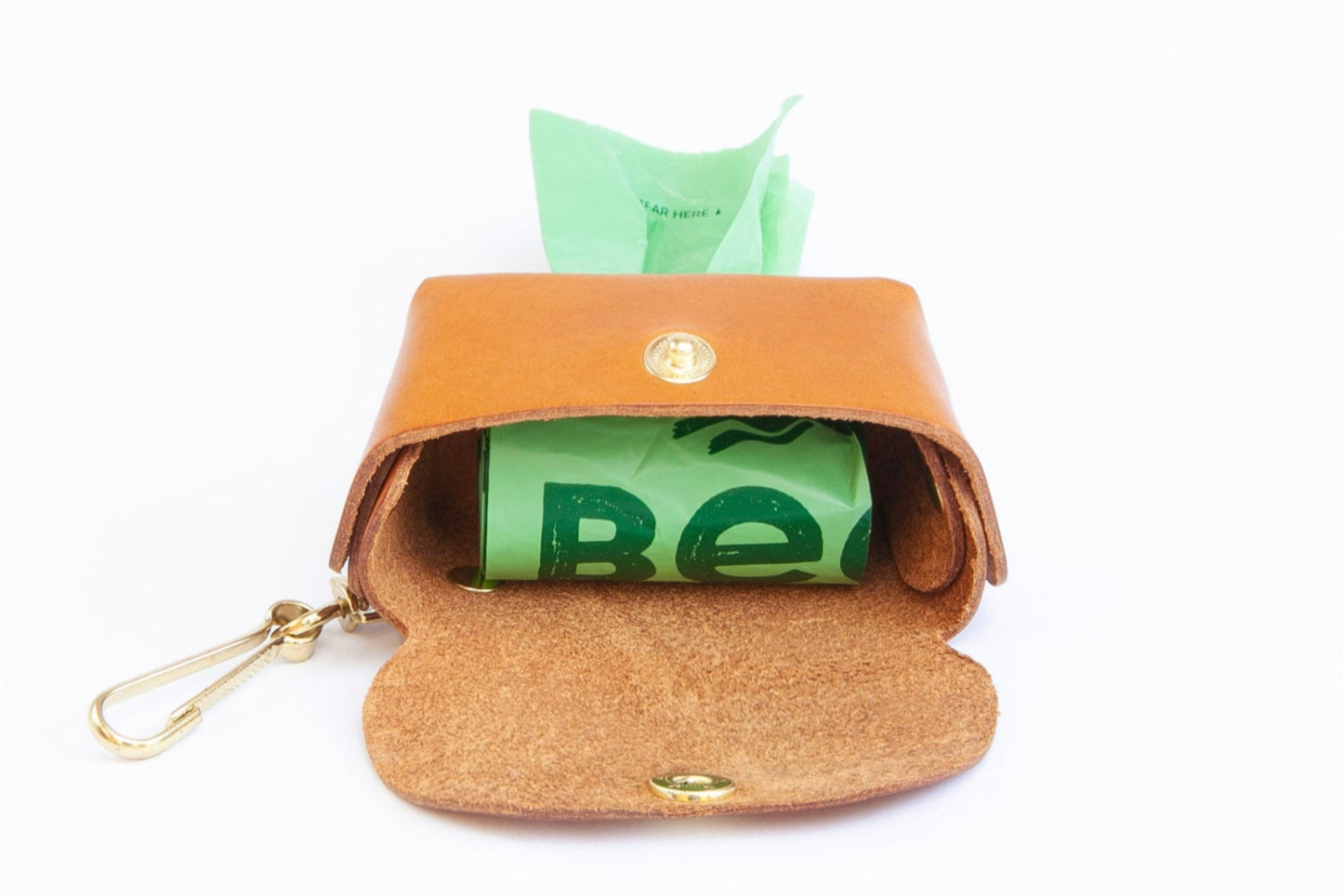 Tan leather poop bag holder open showing roll of bags inside, with pop stud closure, bottom dispensing hole, and brass clip for attaching, made by Cotswold Hipster