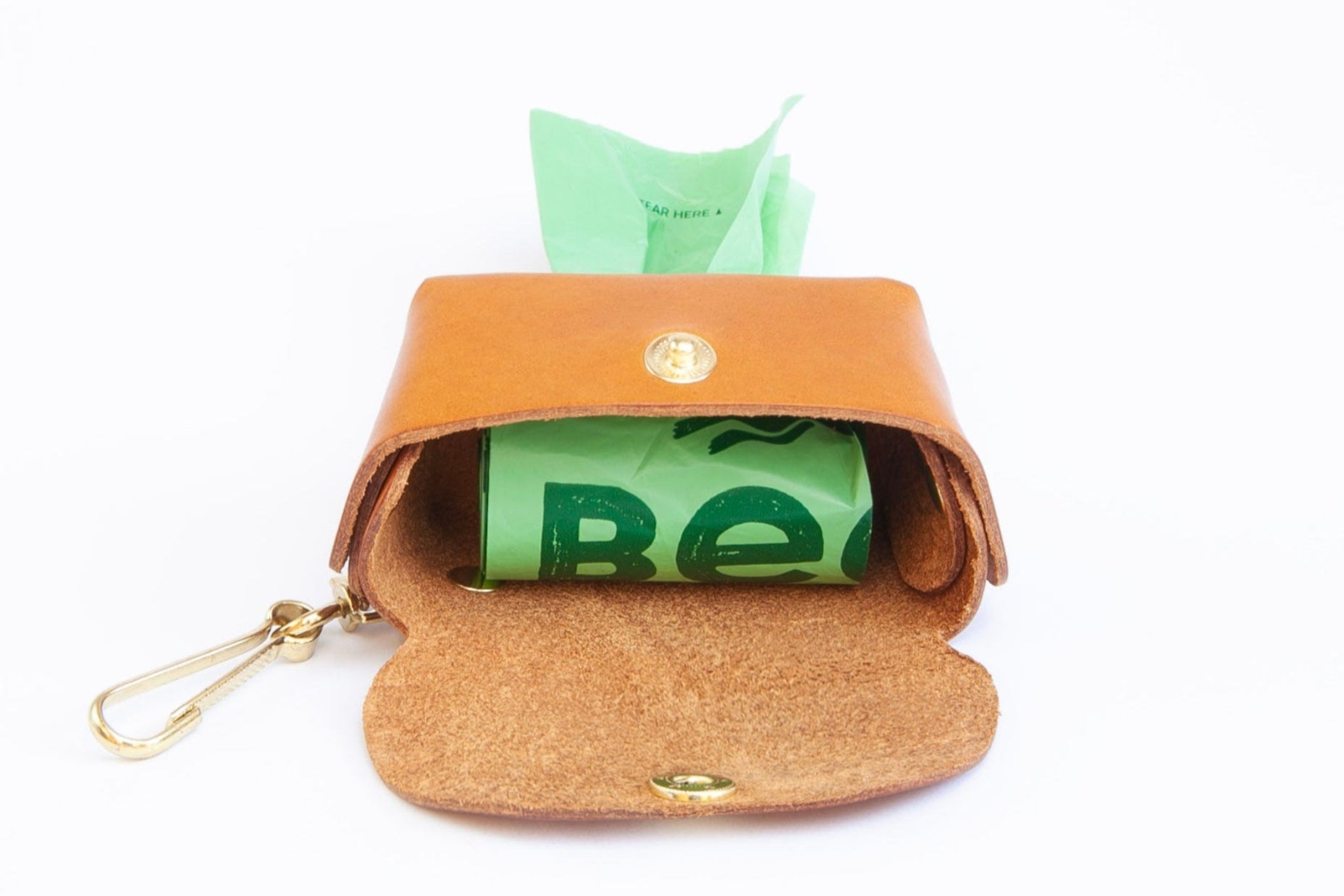 Tan leather poop bag holder open showing roll of bags inside, with pop stud closure, bottom dispensing hole, and brass clip for attaching, made by Cotswold Hipster