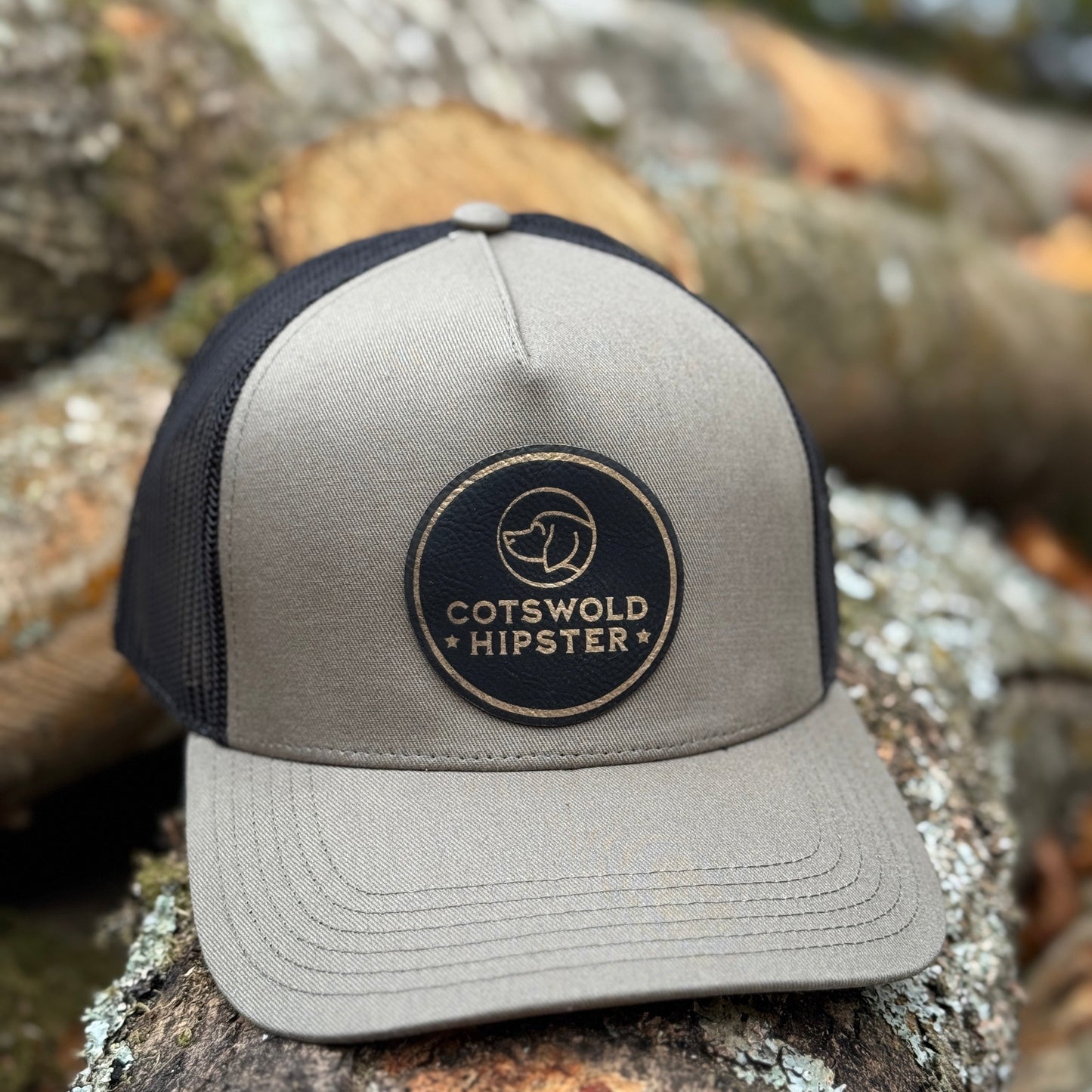 Khaki Field Cap angled on logs in the Cotswolds, highlighting logo patch and mesh panels.