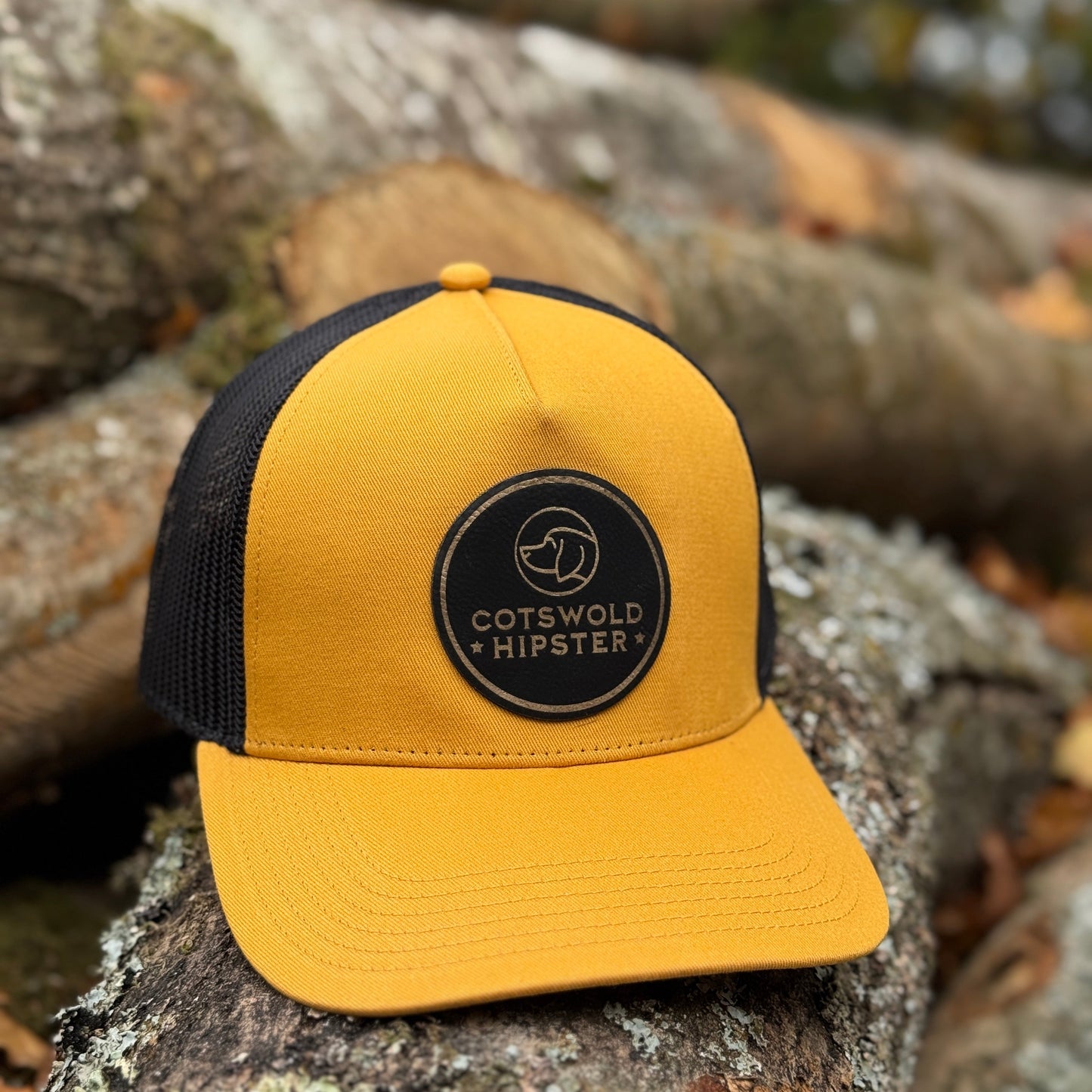 Mustard Field Cap angled on logs in the Cotswolds, highlighting logo patch and mesh panels.