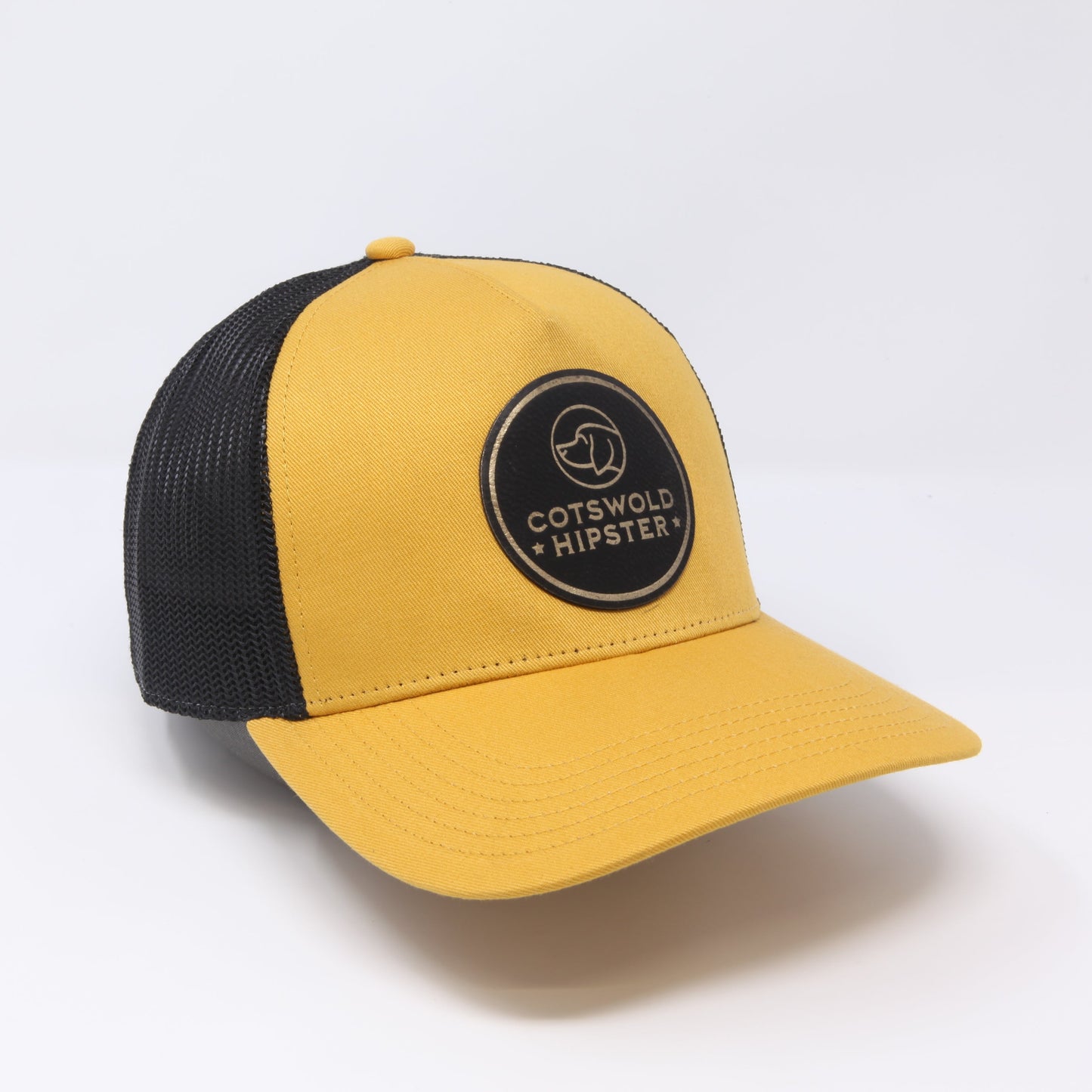 Mustard Field Cap angled to the side on white background, showing leather logo, mesh panels, and snap-back closure.
