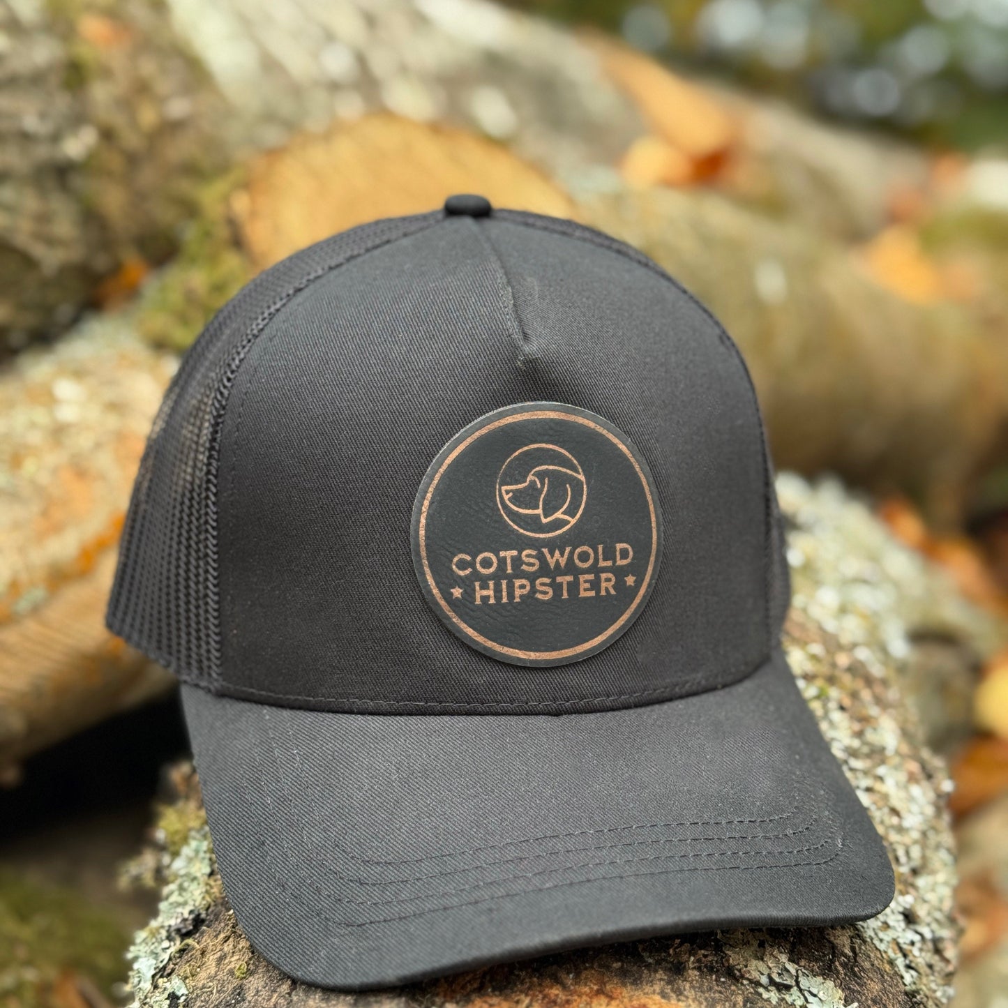 Black Field Cap angled on logs in the Cotswolds, highlighting logo patch and mesh panels.